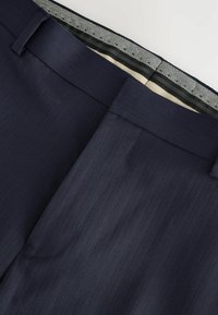 Mornarsko prugaste hlače s glatkom teksturom, koje imaju elegantan pojas i kontrastno unutarnje podstavu s suptilnim uzorkom.