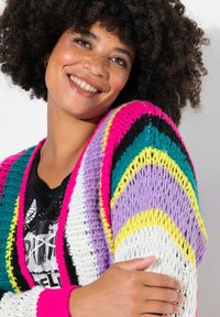 Kleurrijke gebreide cardigan met regenboogstrepen in roze, teal, paars, zwart, wit en geel, met een losse, gebreide textuur.