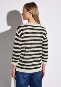 Gestreifter, schwarz-weißer, gestrickter Pullover mit losem Gewebe, drei Viertelärmeln, gerippten Bündchen und Saum, getragen mit blauen Jeans.