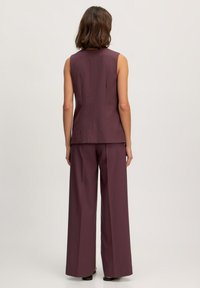 Ärmelloses, tief burgunderfarbenes Top, kombiniert mit weit geschnittenen Hosen in derselben Farbe; glattes Material mit taillierter Passform und subtilen Nähdetails.