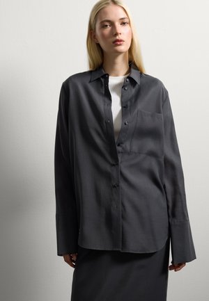 Camicia grigia scura a maniche lunghe, con bottoni, realizzata in un tessuto morbido, dotata di taschino sul petto, vestibilità rilassata e orlo curvo.