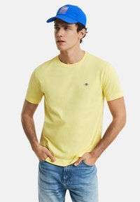 Yellow cotton t-shirt with short sleeves and a round neckline, paired with a blue cap featuring a logo and patch. Light blue denim jeans.