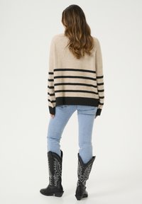 Beige csíkos pulóver fekete vízszintes csíkokkal, világoskék farmerral és fekete díszített cowboy csizmával párosítva. Hátsó nézet.