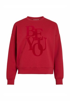 Sweatshirt en coton rouge avec un col rond et des épaules baissées. Présente un grand graphique "SOIS TOI" en tons variés. Texture douce.