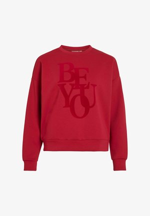 Rød bomullsgenser med rund hals og senkede skuldre. Har et stort tonalt "BE YOU" grafikk i varierende størrelser. Myk tekstur.