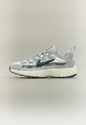 Zapatilla deportiva gris claro con logo de Nike en verde, detalles de malla, suela blanca gruesa y marca "P-6000" en el lateral del talón.