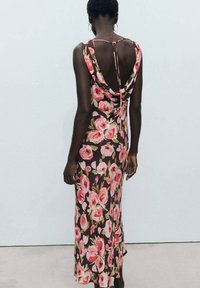 Rochie maxi florală cu bază maro și flori roz, având un spate drapat, bretele subțiri și o siluetă ajustată.