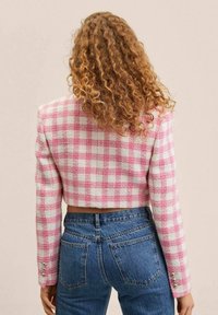 Krátká bunda v růžovo-bílém kostkovaném vzoru, vyrobená z texturované látky se rovnými rukávy a kovovými knoflíky na manžetách.