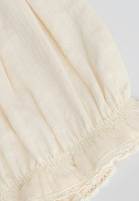 Tissu couleur crème avec une couture élastique froncée et un délicat galon de dentelle le long du bord, montrant une texture douce et légère.