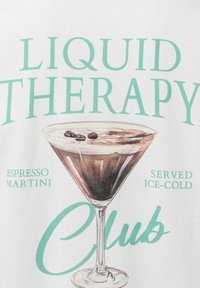 Weißer Stoff mit einem grafischen Design eines Martini-Glases, gefüllt mit einer dunkelbraunen Flüssigkeit, garniert mit Kaffeebohnen und dem Text "LIQUID THERAPY."