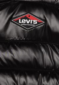 Levi's Expeditionaries logo patch med rødt bjerge-design på sort skinnende quiltet stof, sandsynligvis en jakke.