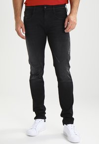Svarta denimjeans med en slim fit, med slitna detaljer på knäna. Bärs med vita sneakers och en röd skjorta.