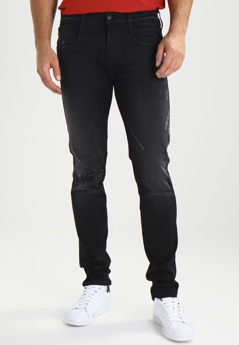 Svarta denimjeans med en slim fit, med slitna detaljer på knäna. Bärs med vita sneakers och en röd skjorta.