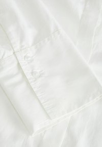 Witte katoenen shirtkraag met een gladde textuur, voorzien van twee transparante knopen en nette stiksels langs de randen.
