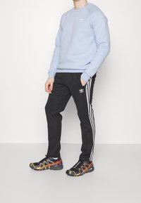 Světle modrý svetr s kulatým výstřihem, černé tepláky s bílými pruhy a logo, a černobílé běžecké boty s texturovanými detaily.