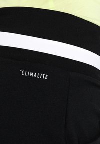 Leggings de sport noirs avec une bande horizontale blanche et le logo "Climalite". Fabriqués en tissu lisse et flexible, adaptés à une utilisation active.