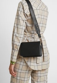 Borsa a tracolla nera in pelle con forma rettangolare, caratterizzata da accessori dorati e una tracolla regolabile. Motivi non visibili.