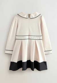Abito crema con maniche lunghe, colletto e rifiniture nere. Presenta una gonna plissettata e un orlo nero. Chiusura con zip sul retro. Tessuto morbido e liscio.
