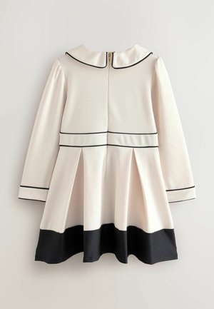 Robe crème à manches longues, col noir et bordure noire. Présente une jupe plissée et un ourlet noir. Fermeture éclair à l'arrière. Texture de tissu lisse.