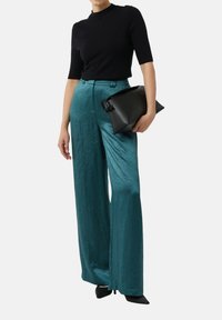 Teal wijde broek in een textiele stof, gecombineerd met een aansluitend zwart kort mouwtop. Houdt een zwart leren clutch vast met een geknoopt accent.