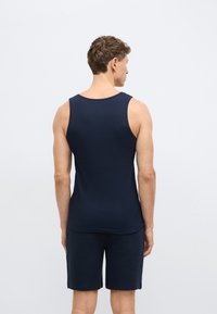 Tmavomodré tielko bez rukávov s rebrovanou textúrou, nosené s tmavomodrými šortkami, ktoré zdôrazňujú priliehavý strih a zaoblený výstrih.