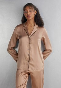 Satin pajamaset i mjuk beige med notch-krage, svart piping och knapplist fram. Långa ärmar och avslappnad passform.