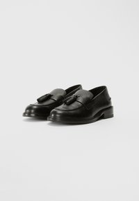 Mocassins en cuir noir avec un bout arrondi, des accents de gland à l'avant et un petit talon carré. Texture lisse et coutures détaillées le long des bords.