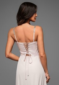 Vestito rosa chiaro con corpetto aderente, dettaglio con lacci sulla schiena e spalline regolabili e decorate. Tessuto morbido e gonna fluida.