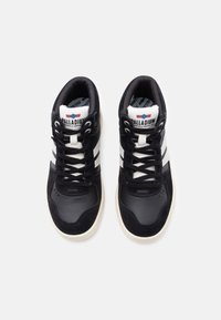 Mustad mustad tossud, millel on nahast ja sametist pealis, valgete triipudega, ümmarguste paeltega ja bränditud keele sildiga.