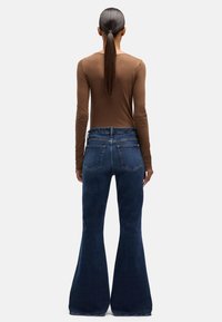 Dżinsy z wysokim stanem i rozszerzanymi nogawkami w ciemnoniebieskim denimi. Posiadają pięć kieszeni, solidny pas i lekko postrzępiony wygląd w okolicy krawędzi.