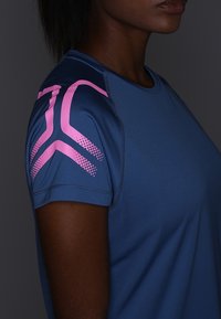 Camiseta deportiva azul de manga corta. Presenta un diseño geométrico rosa en el hombro. Hecha de un material suave y ligero.
