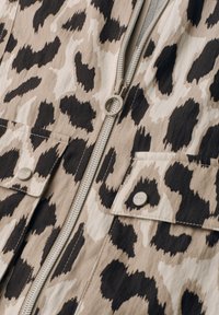 Beige og sort leopardprintstof med sølvlynlås og to lommer med knapper og klap.