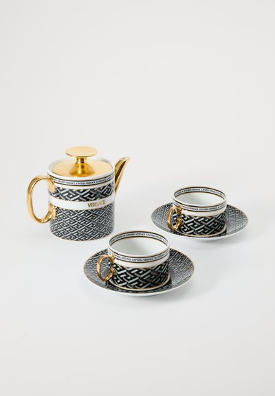 Dzbanek na herbatę oraz dwie filiżanki z podstawkami. Ceramika czarno-biała z geometrycznym wzorem, złotymi akcentami i logo "Versace" na krawędziach.