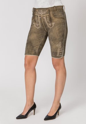 Braune knielange Lederhosen aus Leder mit bestickten Mustern, getragen mit schwarzen High-Heels auf einfarbigem Hintergrund.