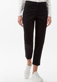 Pantaloni neri a sigaretta con una superficie liscia, caratterizzati da una vita con bottone, tasche laterali e una lunghezza cropped, abbinati a sneaker bianche.