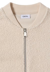 Beige strukturierte Zip-Jacke mit geripptem Kragen und silbernem Reißverschluss, mit einem "CECIL"-Markenlabel im Kragen.