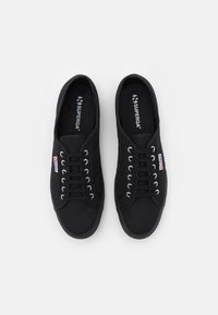 Sneakers neri in tela con suole in gomma rotonde, occhielli argentati e dettagli bianchi con il logo. Lacci piatti e superficie superiore testurizzata.