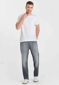 Maglietta bianca a maniche corte con taschino sul petto abbinata a jeans in denim grigio chiaro. I jeans presentano una leggera sbiaditura con taglio dritto. Scarpe da ginnastica bianche.