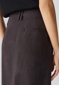 Jupe texturée marron foncé, ajustée, avec une poche arrière et des passants de ceinture, fabriquée à partir d'un tissu léger.