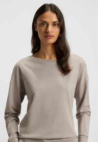 Beige langärmliges Oberteil aus weichem Stoff, mit rundem Ausschnitt und lockerem Schnitt. Glatte Textur mit dezenten Nahtdetails.