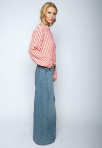 Lange Jeansrock in Hellblau, kombiniert mit einer gemusterten, leichten Bluse in Pink und Orange. Die Bluse hat lange Ärmel und einen abgerundeten Saum.