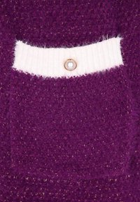 Țesătură texturată de culoare mov, cu un buzunar tricotat și o bandă albă cu nervuri, care prezintă un nasture din perlă. Firele metalice subtile adaugă detaliu.