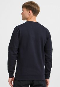 Mørk marineblå hettegenser laget av myk stoff. Har rund hals, lange ermer og en avslappet passform med forsterket søm.