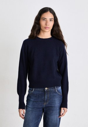 Suéter de lana azul marino con cuello redondo, puños y dobladillo acanalados. Combinado con jeans azules, con una forma ajustada y textura suave.