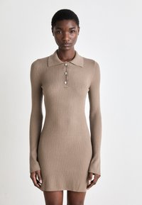 Stripet strikket polokjole i beige med lange ermer, krage og tre knappelukkinger foran. Tekturen på stoffet er glatt.