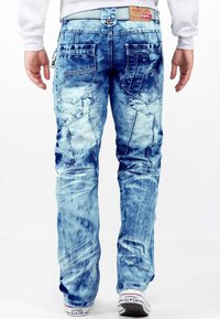 Jeans in denim azzurro chiaro con un lavaggio sbiadito, caratterizzati da vari design di tasche, dettagli cuciti e una vestibilità comoda, indossati con sneakers bianche.