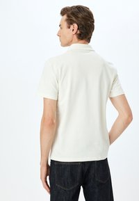 Pikétröja i ljusgräddfärg, kort ärm, tillverkad av ett slätt tyg, med en klassisk krage och minimala sömnadsdetaljer. Kombination med mörka jeans.