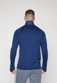 Dunkelblauer Langarmpullover mit hohem Kragen, aus glattem Stoff. Verfügt über ein figurbetontes Design und kontrastierende weiße Streifen an den Ärmeln.