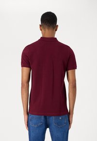 Maroon short-sleeve polo shirt with a collar, featuring a smooth texture. Worn with blue denim jeans, showing the back view.