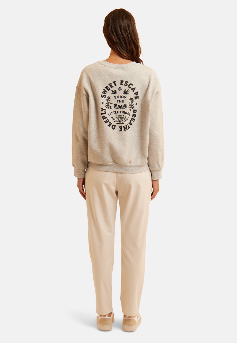 Sudadera de algodón gris claro con diseño de texto negro en la parte posterior, combinada con pantalones beige y zapatos claros. Ajuste relajado, estilo simple.